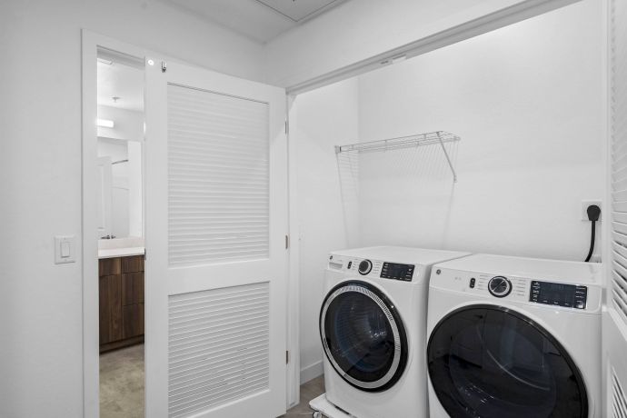 Mesa Vista Affordable Apartments with Modern laundry room with a washer and dryer, white walls, and a sliding door partially open.