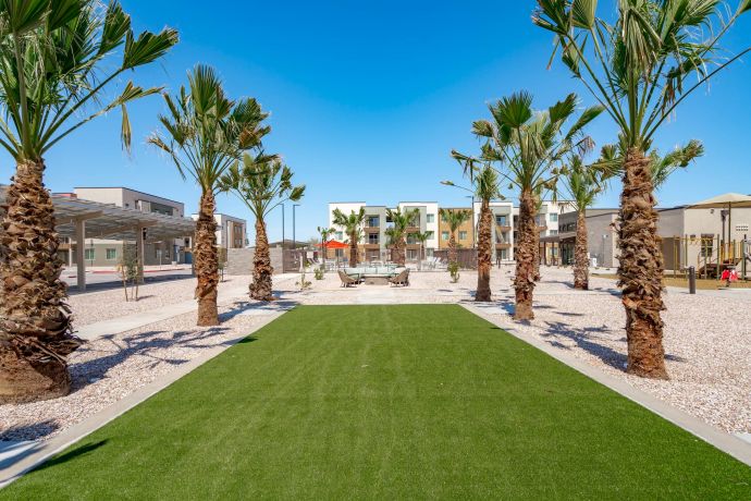 Mesa Vista Affordable Apartments with A row of palm trees lines a green lawn in front of modern apartment buildings under a clear blue sky.