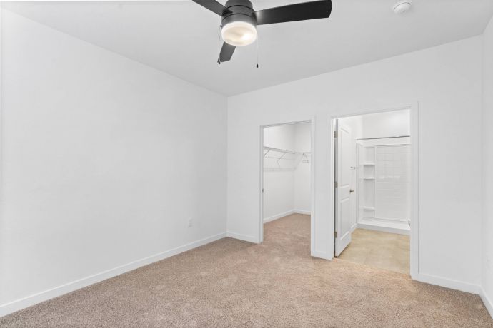 Mesa Vista Affordable Apartments with Empty white bedroom with beige carpet, ceiling fan, walk-in closet, and bathroom.