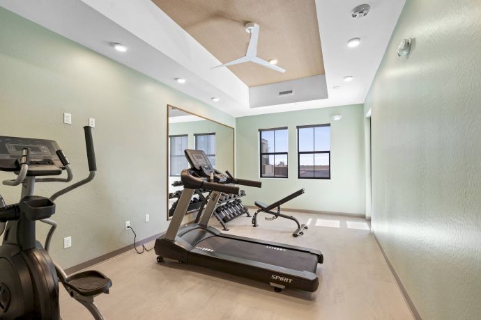 Mesa Vista Affordable Apartments with Small home gym with a treadmill, exercise bike, weights, bench, large mirror, and green walls.
