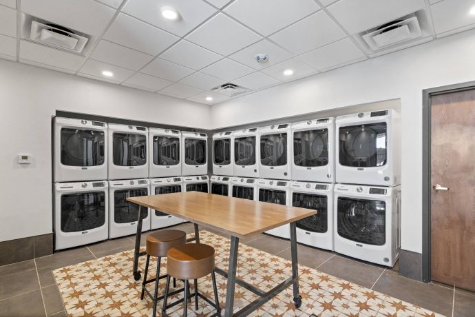 Mesa Vista Affordable Apartments with Modern laundry room with stacked washers and dryers, a wooden table, and two stools on a patterned rug.