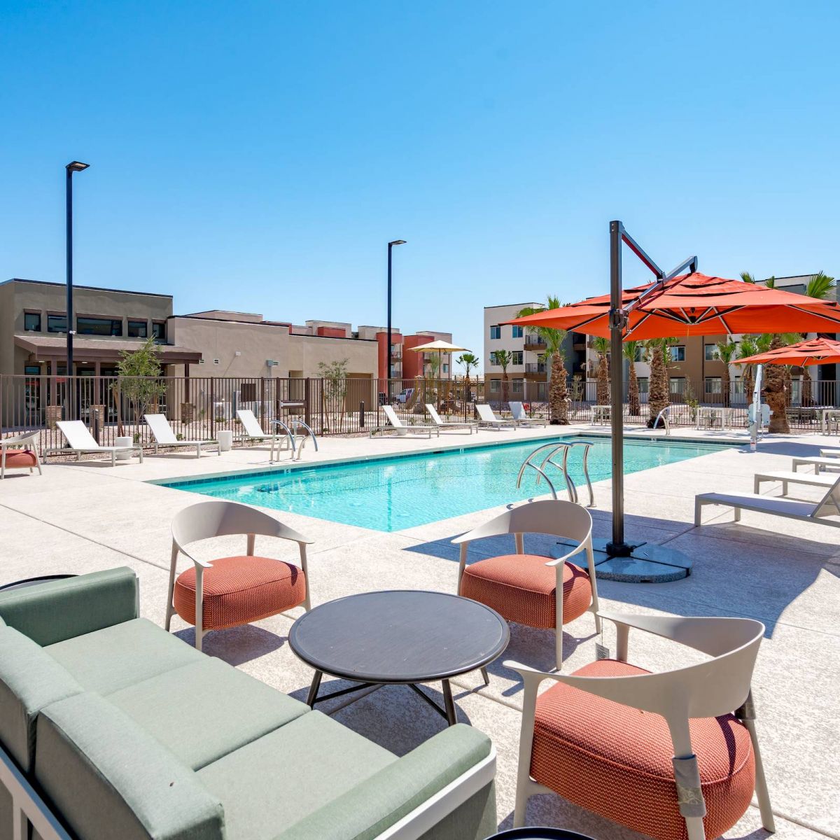 Mesa Vista Affordable Apartments with Outdoor pool area with lounge chairs, orange umbrellas, and modern apartment buildings in the background.