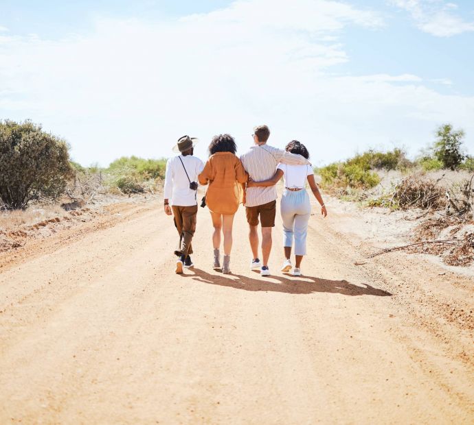 Mesa Vista Affordable Apartments with Four friends walk arm in arm down a sunny dirt road surrounded by bushes and trees.