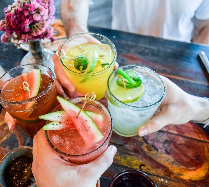 Mesa Vista Affordable Apartments with Four people toast with colorful cocktails garnished with fruit, around a rustic wooden table.