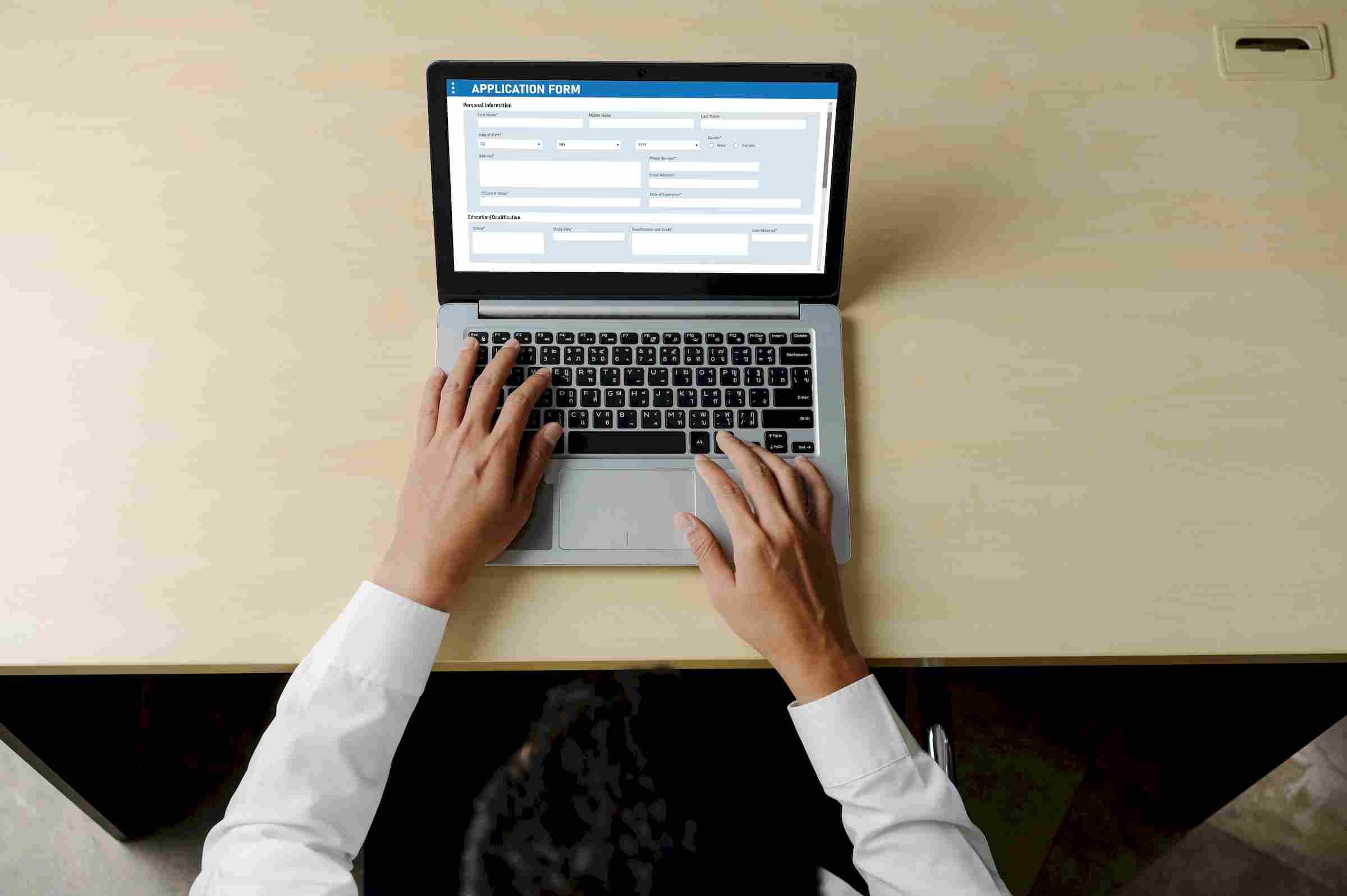 Affordable Apartments with Person filling out an online application form on a laptop at a desk, viewed from above.